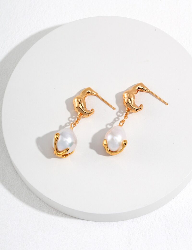 A pair of elegant  drop earrings with a swan design at the top and a dangling freshwater pearl at the bottom, displayed on a white circular surface. Elegant pearl jewelry