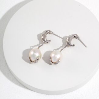 A pair of elegant earrings featuring flamingo-shaped hooks holding large natural pearls, displayed on a circular white platform with a subtle texture. Elegant pearl jewelry