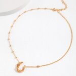 Gold pearl jewelry bracelet featuring a delicate chain with a crescent moon and star charm, displayed on a light textured surface.