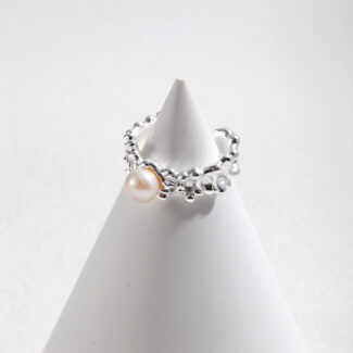 A  ring showcased on a white cone-shaped display against a light gray background. The ring features intricate metalwork with small embellishments. Elegant pearl jewelry