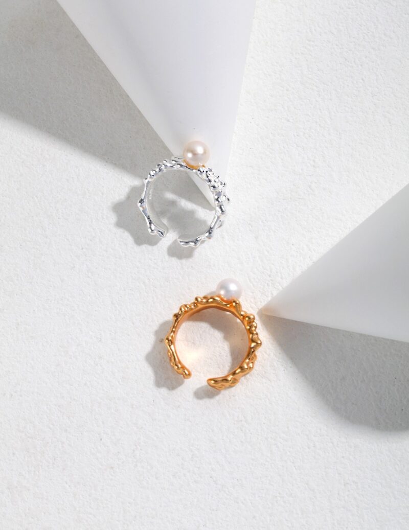 Two elegant  rings, one silver and one gold pearl jewelry, displayed on a white surface intersected by soft geometric shadows, creating a minimalist and refined presentation. Elegant pearl jewelry