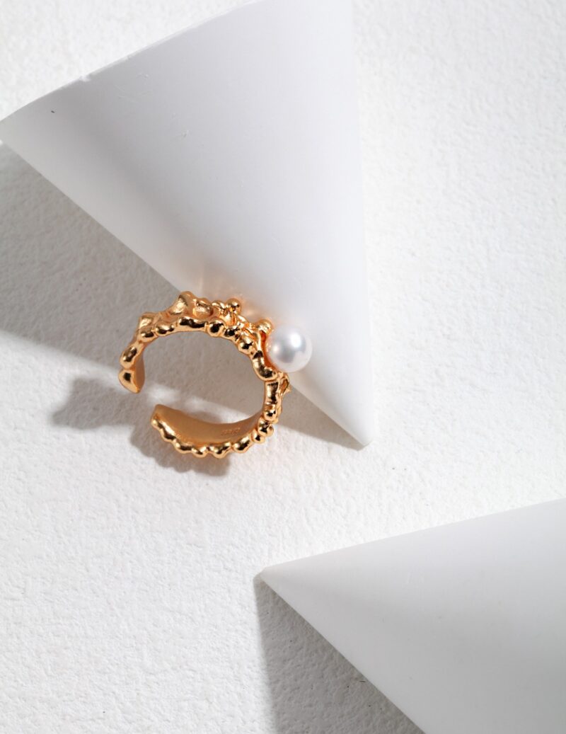 A adorned with a natural pearl, set against a white geometric background with contrasting shadows. Elegant pearl jewelry