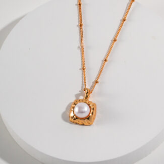 A  necklace with a heart-shaped pendant featuring a central freshwater pearl, displayed on a white cylindrical stand against a light background. Elegant pearl jewelry