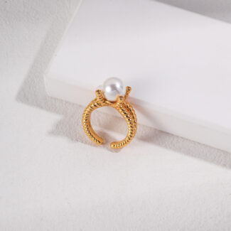 A ring with a textured band and a large freshwater pearl set at the top, displayed on a white surface beside a rectangular block. Elegant pearl jewelry