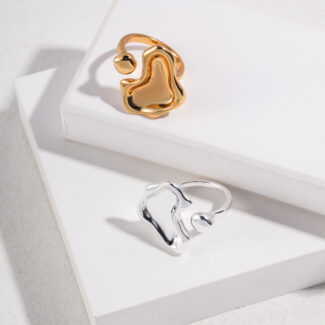 Two rings, one gold and one silver, both featuring pearl jewelry, placed on a white rectangular box with a textured background, highlighted by shadows. Elegant pearl jewelry