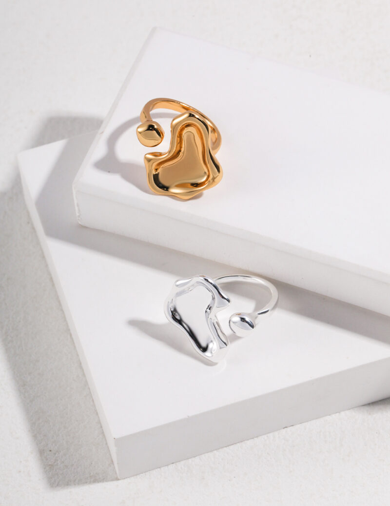 Two rings, one gold and one silver, both featuring pearl jewelry, placed on a white rectangular box with a textured background, highlighted by shadows. Elegant pearl jewelry