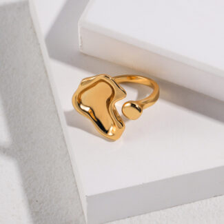 A glossy, gold pearl jewelry ring rests on a white geometric platform with a shadow casting over a textured surface, highlighted by natural light. Elegant pearl jewelry