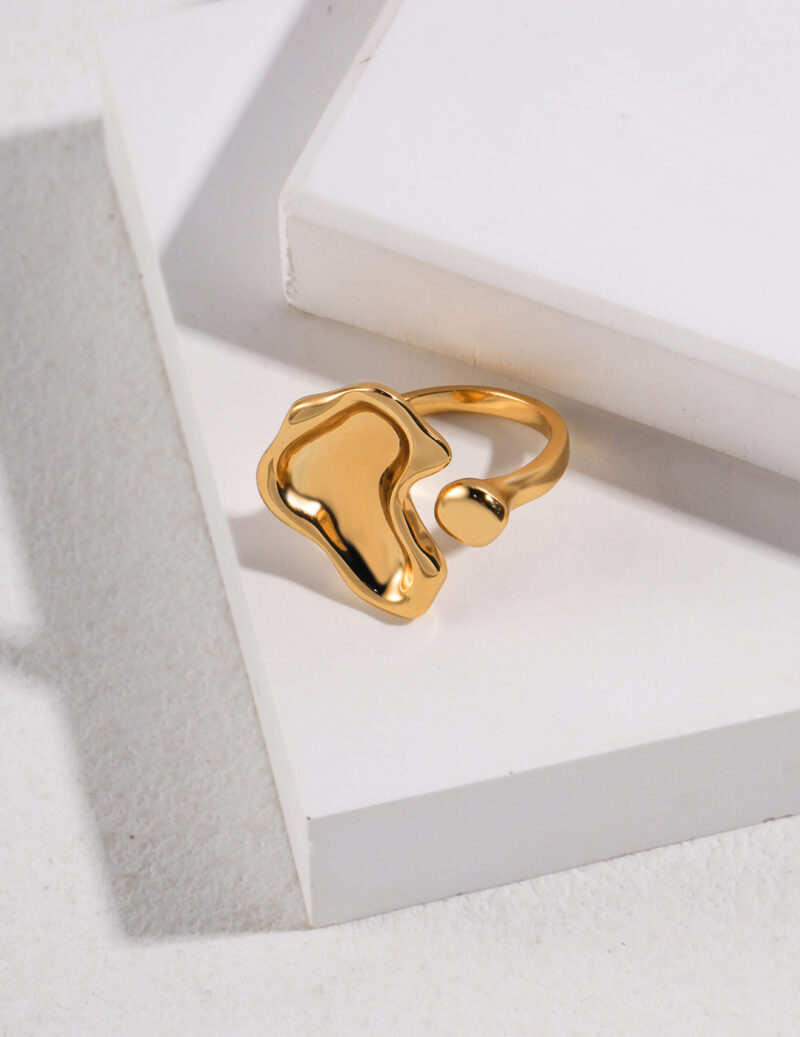 A glossy, gold pearl jewelry ring rests on a white geometric platform with a shadow casting over a textured surface, highlighted by natural light. Elegant pearl jewelry