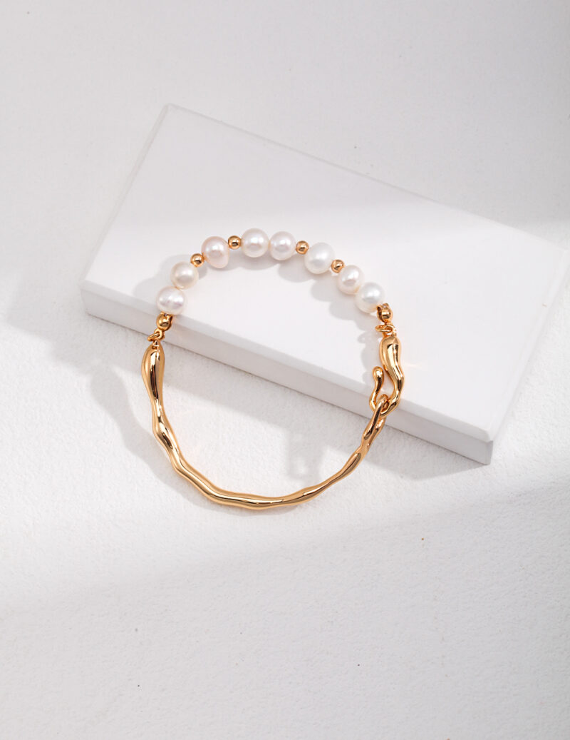 A freshwater pearl bracelet with a gold chain detail, elegantly placed on against a light gray background. Elegant pearl jewelry