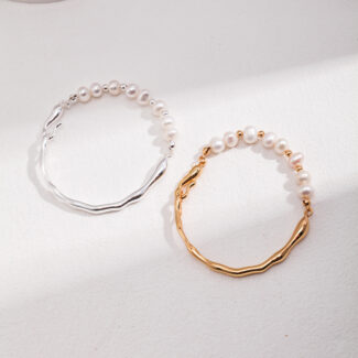 Sentence with product name: Two bracelets lying on a light surface, one with a sterling silver chain and the other with a gold chain, both featuring a wavy design. Elegant pearl jewelry