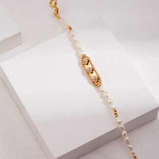 An elegant  bracelet with a gold filigree centerpiece, draped over a white marble block against a light background. Elegant pearl jewelry