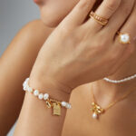 A close-up of a woman's hand touching her chin, showcasing elegant bracelets and rings. Elegant pearl jewelry