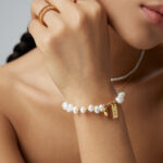 Close-up of a woman's hand adorned with elegant Swarovski crystal rings and a bracelet, touching her chin, showcasing the crystal jewelry against a neutral background. Elegant pearl jewelry