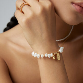 Close-up of a woman's hand adorned with elegant Swarovski crystal rings and a bracelet, touching her chin, showcasing the crystal jewelry against a neutral background. Elegant pearl jewelry