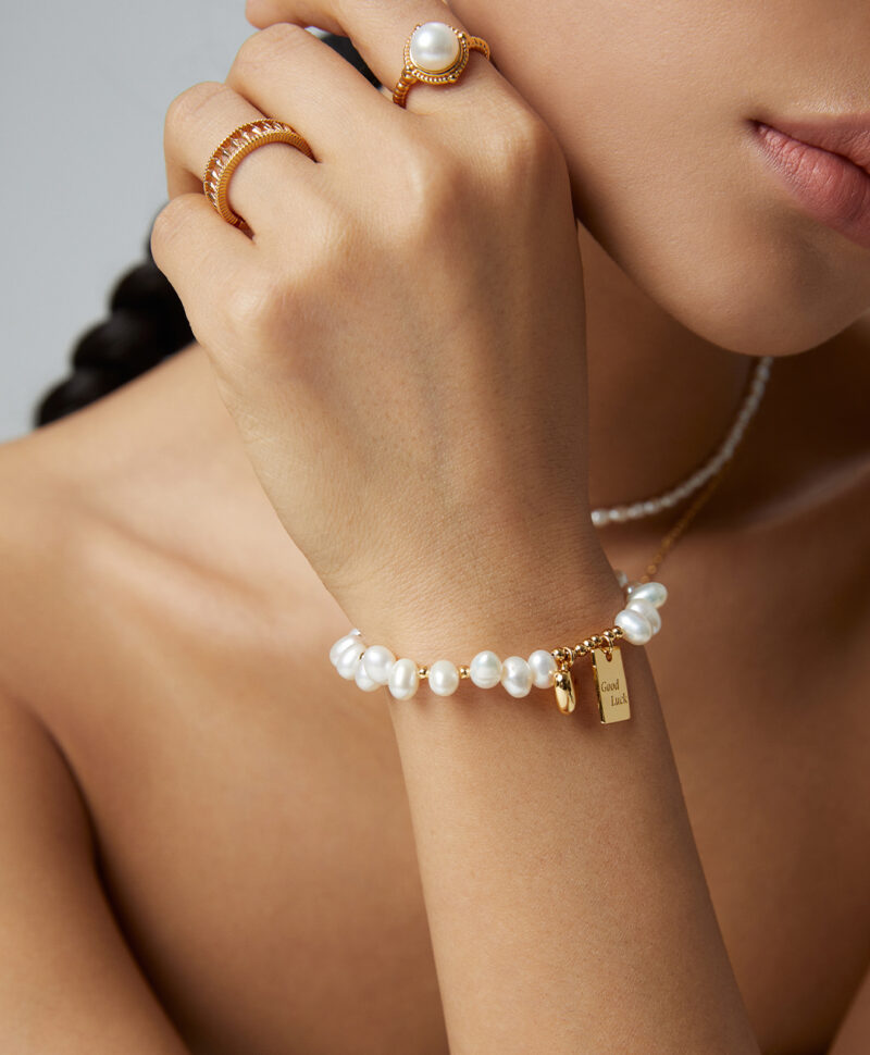 Close-up of a woman's hand adorned with elegant Swarovski crystal rings and a bracelet, touching her chin, showcasing the crystal jewelry against a neutral background. Elegant pearl jewelry