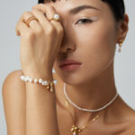 Close-up of a woman with elegant Desiree freshwater pearl jewelry, showcasing a bracelet, rings, and necklace. She has subtle makeup and a contemplative expression. Elegant pearl jewelry