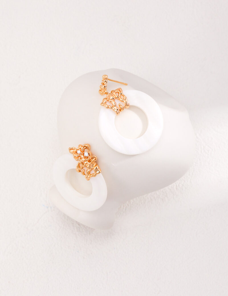 A pair of elegant rings with a floral design incorporating freshwater pearls, connected to large white circular pendants, displayed on a white mannequin bust with a textured background. Elegant pearl jewelry