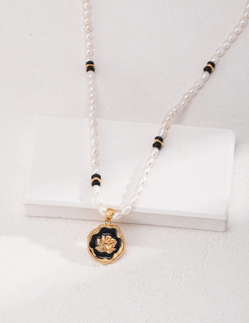 Elegant freshwater pearl necklace with black and gold accents, featuring a prominent gold pendant with a flower design. Elegant pearl jewelry