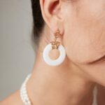 Close-up of a woman's ear and neck, showcasing an intricate earring, paired with a natural pearl necklace, against a neutral background. Elegant pearl jewelry