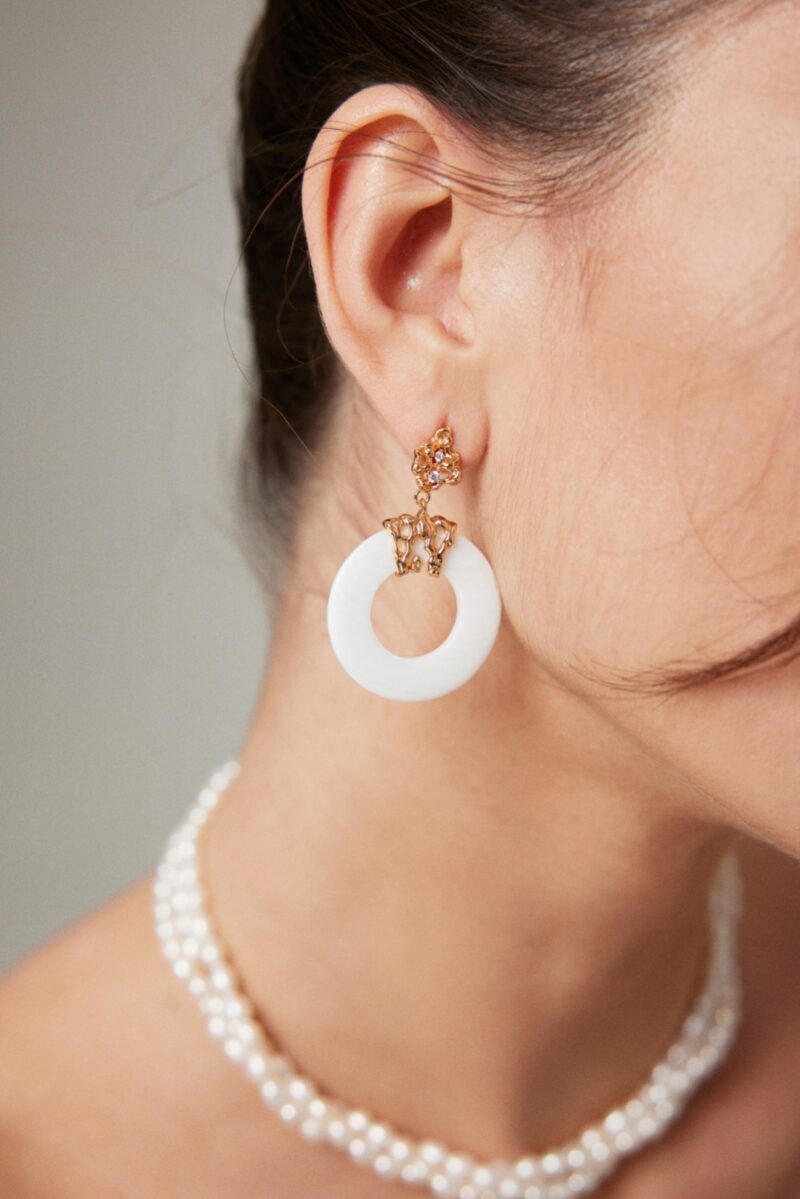 Close-up of a woman's ear and neck, showcasing an intricate earring, paired with a natural pearl necklace, against a neutral background. Elegant pearl jewelry