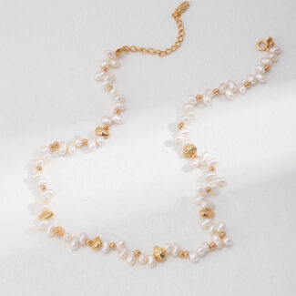 A necklace elegantly arranged on a light grey surface, featuring interspersed gold shell-shaped charms, with an adjustable chain visible. Elegant pearl jewelry