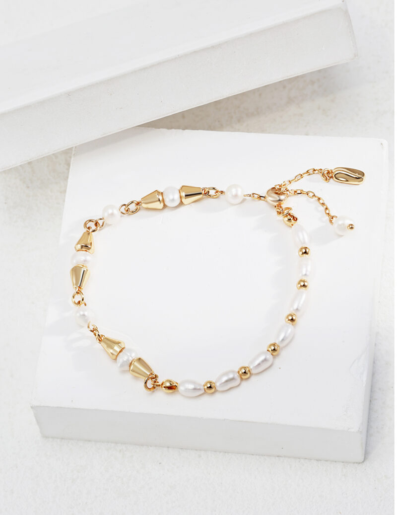 An elegant bracelet with gold accents displayed on a white surface. The bracelet features a mix of large and small pearls interspersed with shiny gold beads and clasps. Elegant pearl jewelry