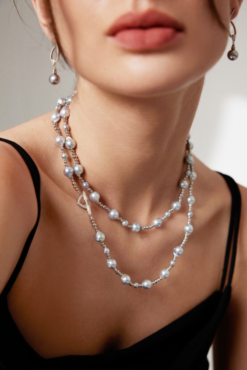 Close-up of a woman wearing an elegant necklace and matching earrings, focusing on the jewelry and the lower part of her face. Elegant pearl jewelry