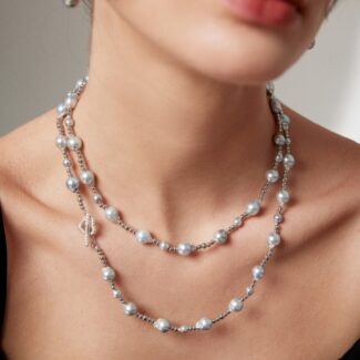 Close-up of a woman wearing a  necklace with a key pendant, and matching earrings, against a soft grey background. Only her neck and lower face are visible. Elegant pearl jewelry