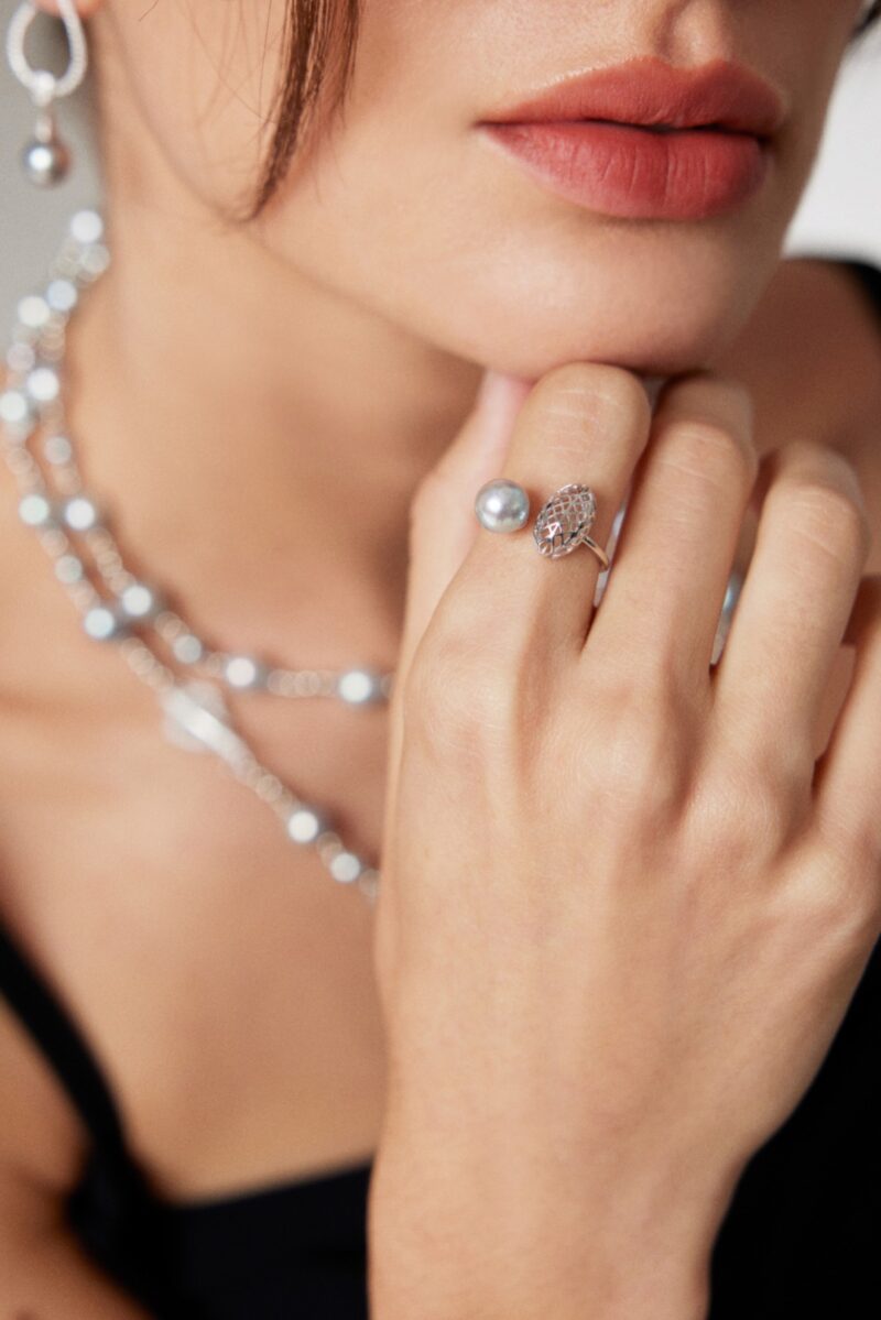 A close-up image of a woman adorned with elegant jewelry, featuring layered pearl necklaces and gold pearl jewelry, focusing on her hand touching her chin