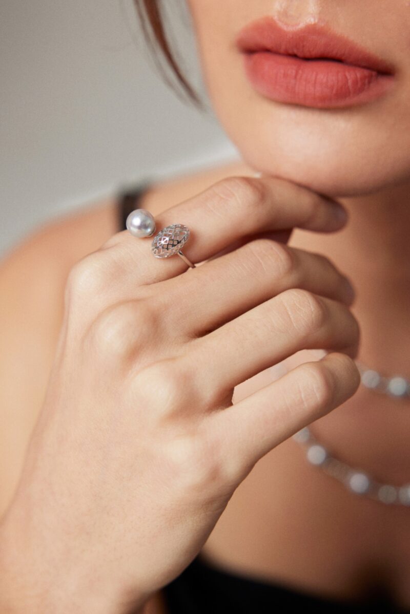 Close-up of a woman's lower face and hand, showcasing a ring and silver necklace, focusing on the elegant details of the jewelry and her pink lipstick. Elegant pearl jewelry