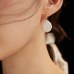 Close-up of a woman's ear wearing a earring featuring a freshwater pearl on a black background. Elegant pearl jewelry