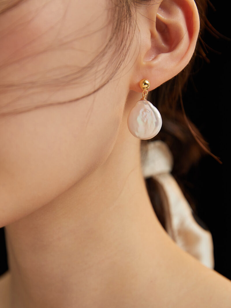 Close-up of a woman's ear wearing a earring featuring a freshwater pearl on a black background. Elegant pearl jewelry