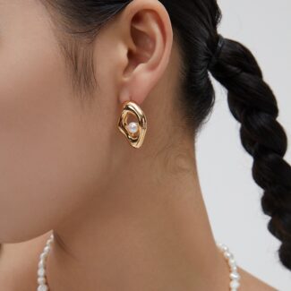 Close-up view of a woman wearing a large gold hoop earring with a freshwater pearl detail, featuring a side profile showing her braided hair and  necklace. Elegant pearl jewelry