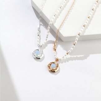 Two elegant pendants with large freshwater pearl pendants, one silver and one gold, resting on a white surface with a shadow cast by natural light. Elegant pearl jewelry