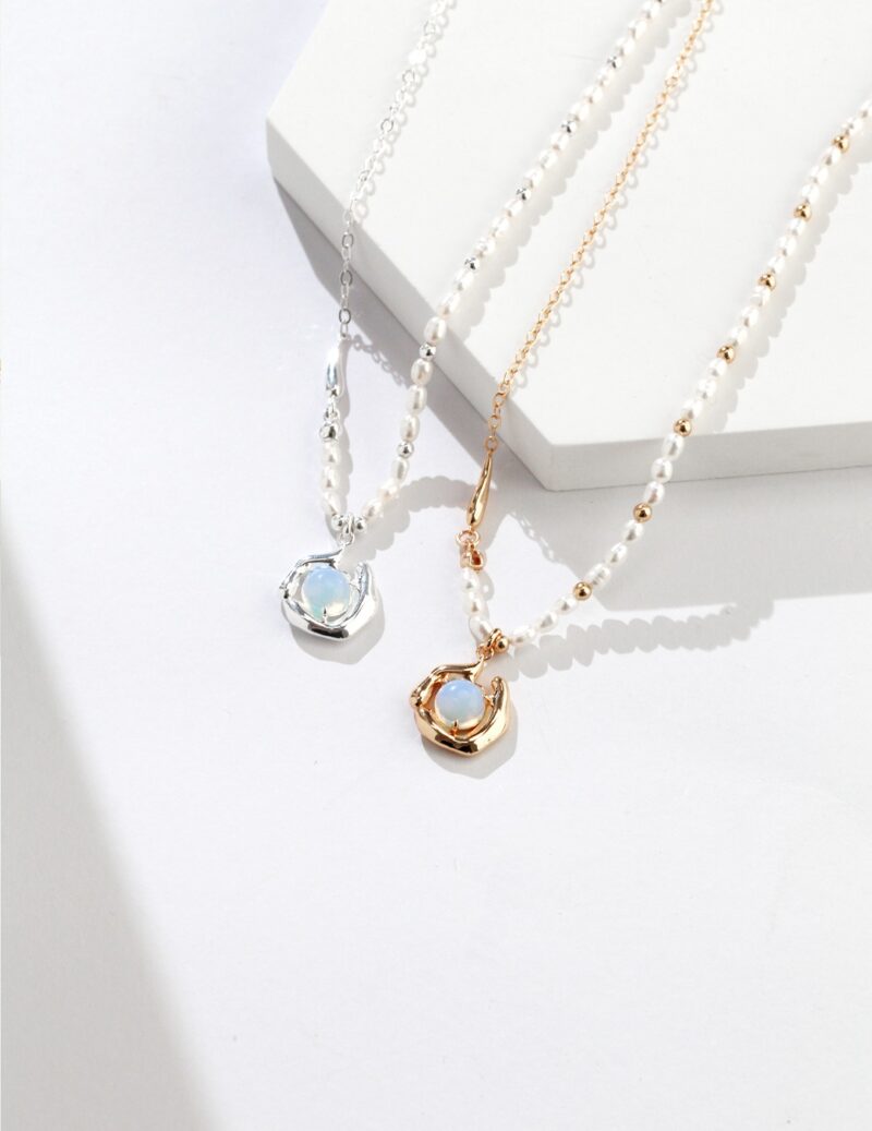 Two elegant pendants with large freshwater pearl pendants, one silver and one gold, resting on a white surface with a shadow cast by natural light. Elegant pearl jewelry