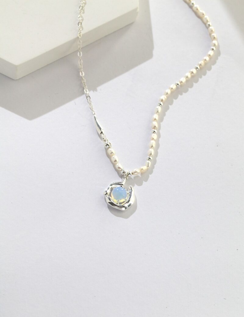 A necklace with a sterling silver chain, featuring a single large pendant. The necklace is set against a plain, light grey background that enhances its elegance. Elegant pearl jewelry