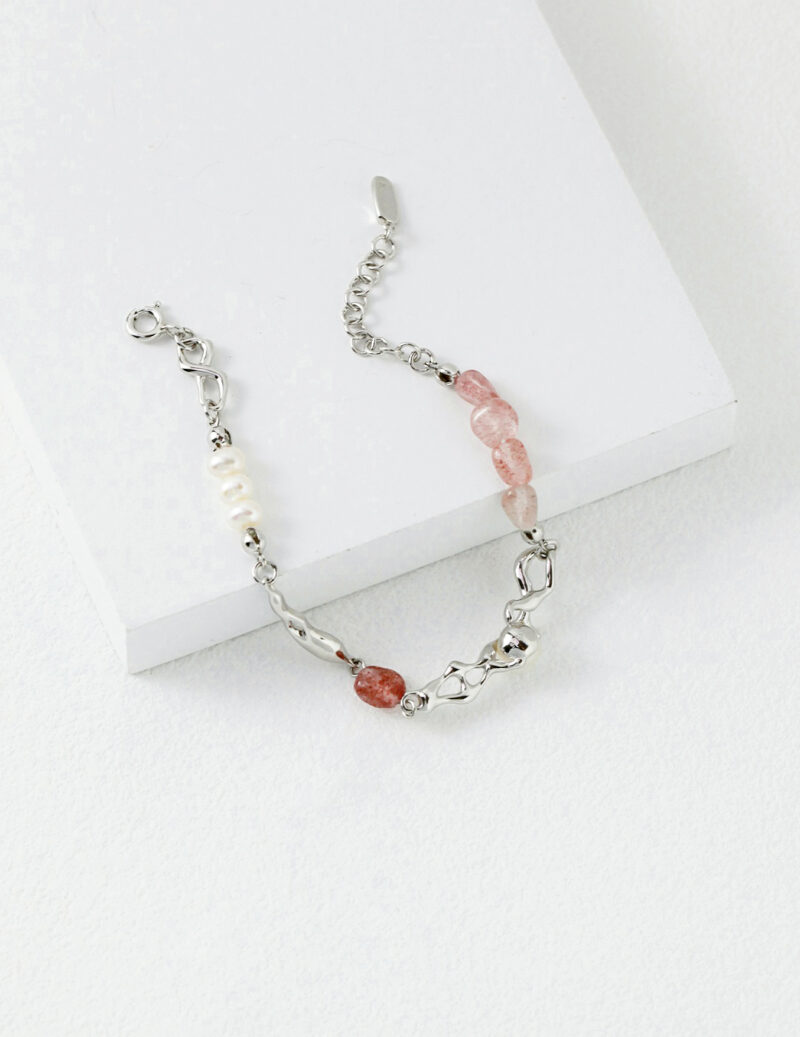 A delicate bracelet featuring a combination of pink and white beads with varying textures, complemented by chain links, displayed on a white box. Elegant pearl jewelry