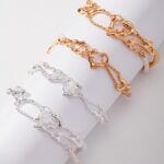 Three delicate bracelets displayed on a cylindrical white holder, featuring intricate link designs in gold pearl jewelry and sterling pearl jewelry colors. Elegant pearl jewelry