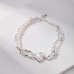 A bracelet with heart-shaped links and sterling pearl jewelry accents laid on a white surface under soft lighting. Elegant pearl jewelry