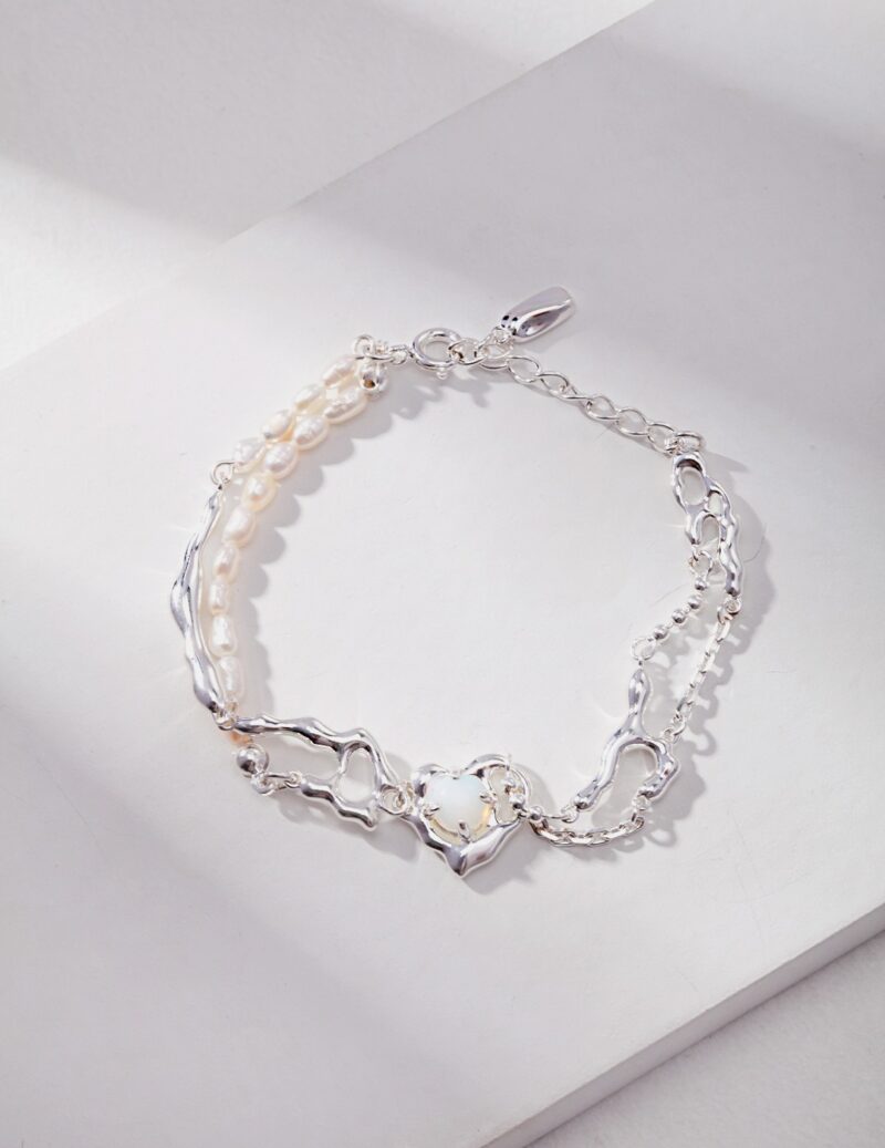 A bracelet with heart-shaped links and sterling pearl jewelry accents laid on a white surface under soft lighting. Elegant pearl jewelry