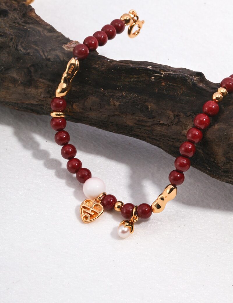 A richly colored bead bracelet adorned with a white bead, a natural pearl, and gold charms, elegantly displayed on a textured piece of driftwood against a light background. Elegant pearl jewelry