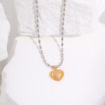 Pearl chain necklace with a gold heart-shaped pendant displayed artistically on white textured rocks. The pendant has a glossy finish, providing a striking contrast against the matte background and is adorned with pearl Elegant pearl jewelry