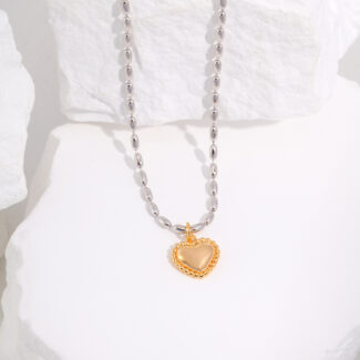 Pearl chain necklace with a gold heart-shaped pendant displayed artistically on white textured rocks. The pendant has a glossy finish, providing a striking contrast against the matte background and is adorned with pearl Elegant pearl jewelry