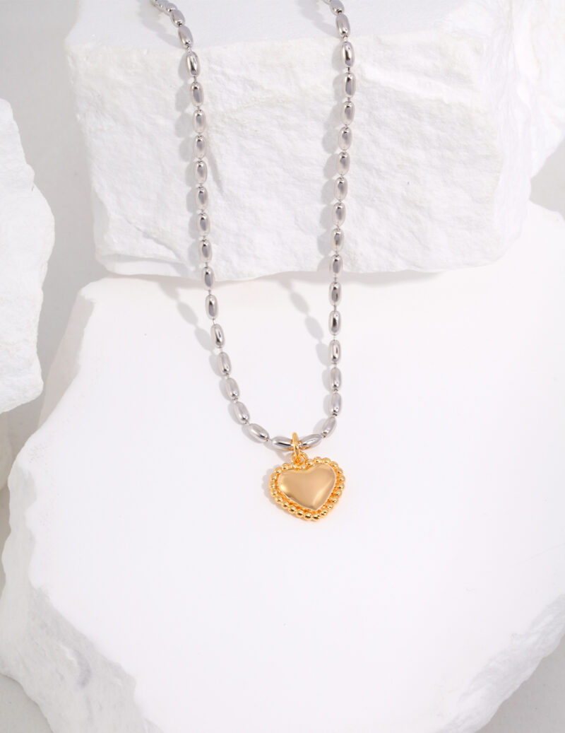 Pearl chain necklace with a gold heart-shaped pendant displayed artistically on white textured rocks. The pendant has a glossy finish, providing a striking contrast against the matte background and is adorned with pearl Elegant pearl jewelry