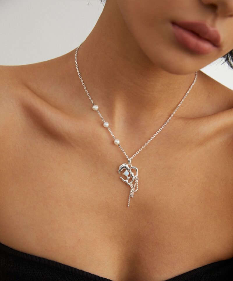 Close-up of a woman wearing delicate jewelry with natural pearls and a heart key pendant, focusing on the necklace against her skin. Elegant pearl jewelry