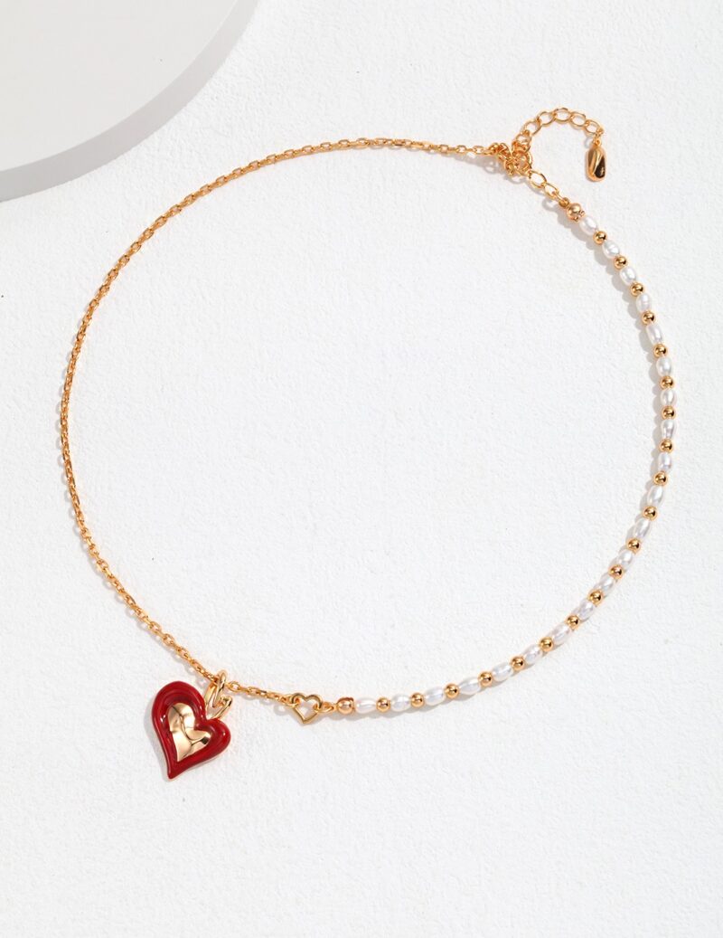 Gold chain bracelet featuring pearls and a red heart-shaped charm, displayed on a white surface with soft shadows. Elegant pearl jewelry