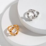 Two elegant rings with freshwater pearl centers placed on a circular display stand, one ring is gold-colored and the other is silver-colored, both feature intricate designs. Elegant pearl jewelry