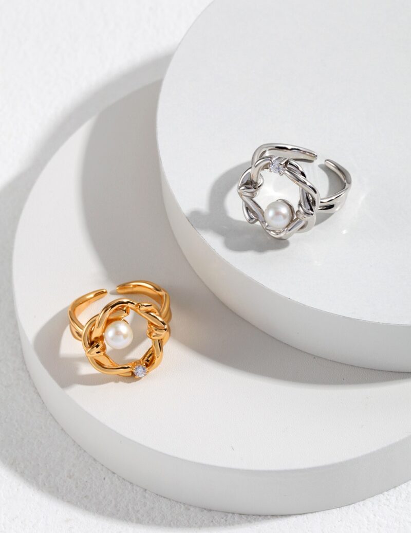 Two elegant rings with freshwater pearl centers placed on a circular display stand, one ring is gold-colored and the other is silver-colored, both feature intricate designs. Elegant pearl jewelry