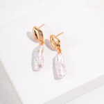 A pair of elegant earrings featuring hoops and dangling freshwater pearls, displayed on a white surface under soft lighting. Elegant pearl jewelry