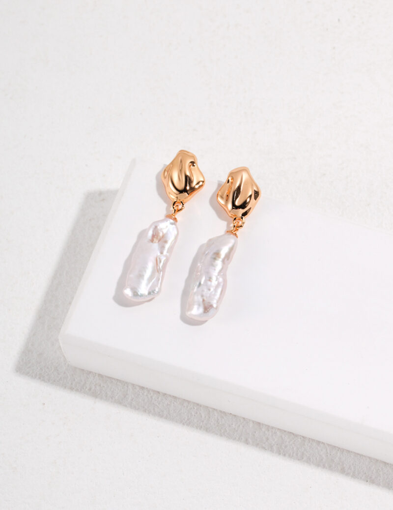 A pair of elegant earrings with rose gold metal clasps and natural pearl pendants, displayed on a white surface. Elegant pearl jewelry